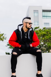 a man in a red and black hoodie sitting on a wall